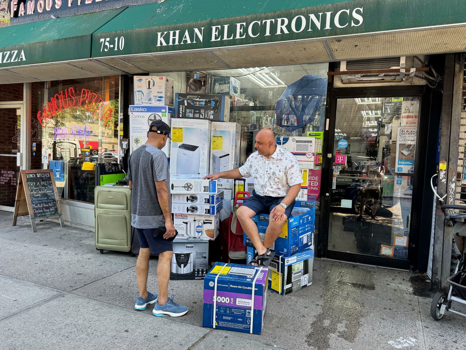 Mudassar Khan, right, talks with a customer while sitting outside his electronics store with air conditioners and fans for sale on display, Tuesday, June 24, 2025, in New York. (AP Photo/Cedar Attanasio)