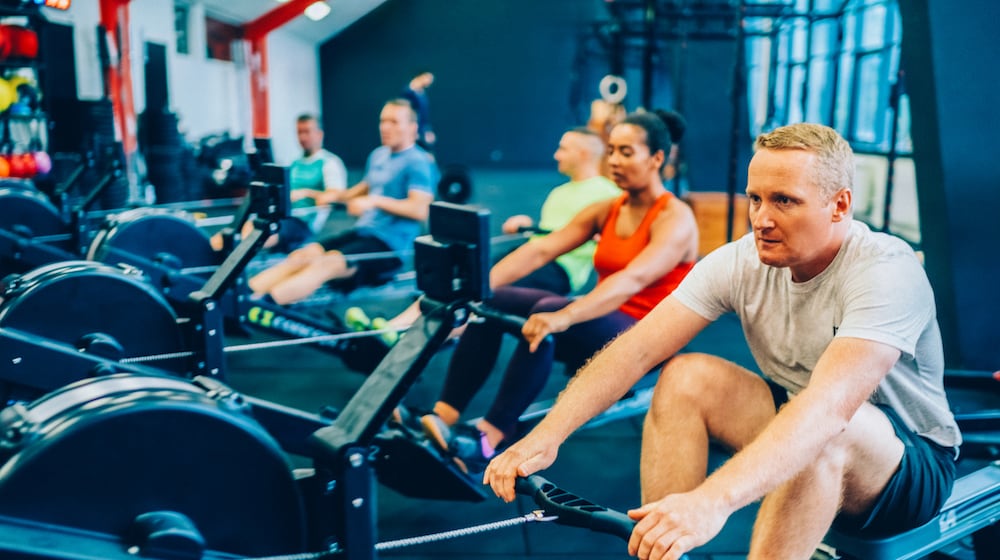 A group of individuals work out together on indoor rowing machines in a modern gym. ISTOCK