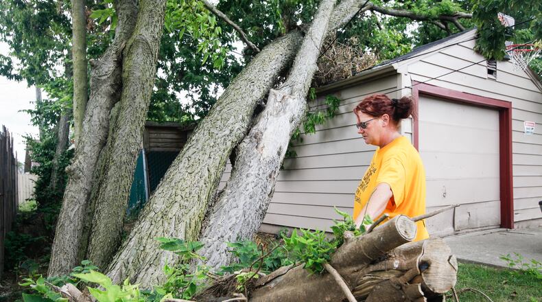 A large tree continues to lean precariously over Nicole Sapp’s garage behind her Brandt Street home in Dayton. She and husband David got bids to have it removed, but the lowest at $2,000 was still more than the family of six can afford right now, she said. “It’s just going to sit there. I don’t know what to do with it,” she said. CHRIS STEWART / STAFF