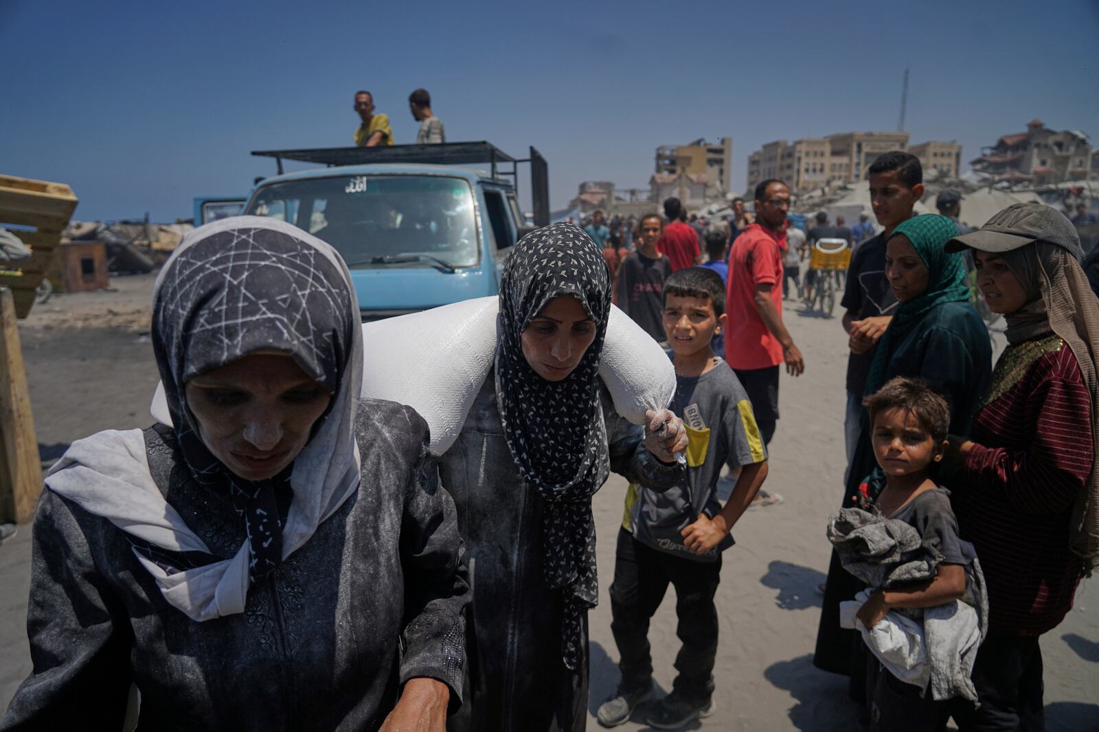 Iman Shabat, a mother of five carries a sack of flour unloaded from a humanitarian aid convoy that reached Gaza City from the northern Gaza Strip, Tuesday, July 22, 2025. (AP Photo/Jehad Alshrafi)