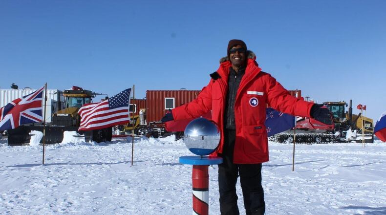 Capt. Michael Nayak at the Ceremonial South Pole with the South Pole Traverse in the background. Several groups of trucks, bulldozers and Sno-Cats (tracked vehicles for snowy conditions) pull massive sleds with supplies from McMurdo Station to the South Pole Station. Each sled holds 20,000 gallons, or 140,000 pounds, of jet fuel. Every year, workers rebuild the thousand mile-road that supports this journey. (Courtesy photo)