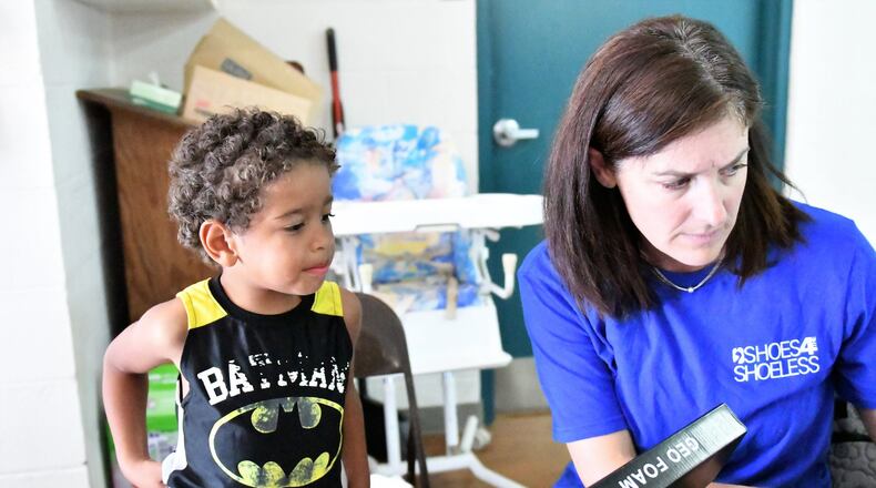 Liz Sonnanstine, a volunteer with Shoes for the Shoeless in Miami County, helps a boy in Bethel Twp. during a recent delivery of shoes and socks. CONTRIBUTED