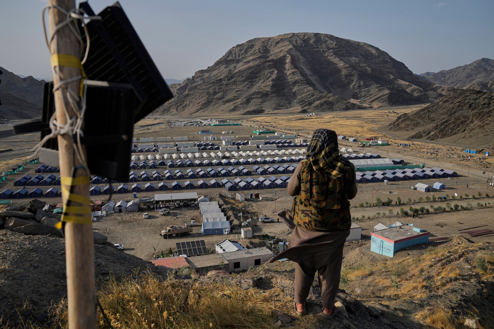 A Taliban fighter stands on a hill overlooking a camp housing Afghan refugees who have been repatriated from Pakistan, near the Pakistan-Afghanistan border, in Torkham, Afghanistan, Saturday, May 31, 2025. (AP Photo/Ebrahim Noroozi)