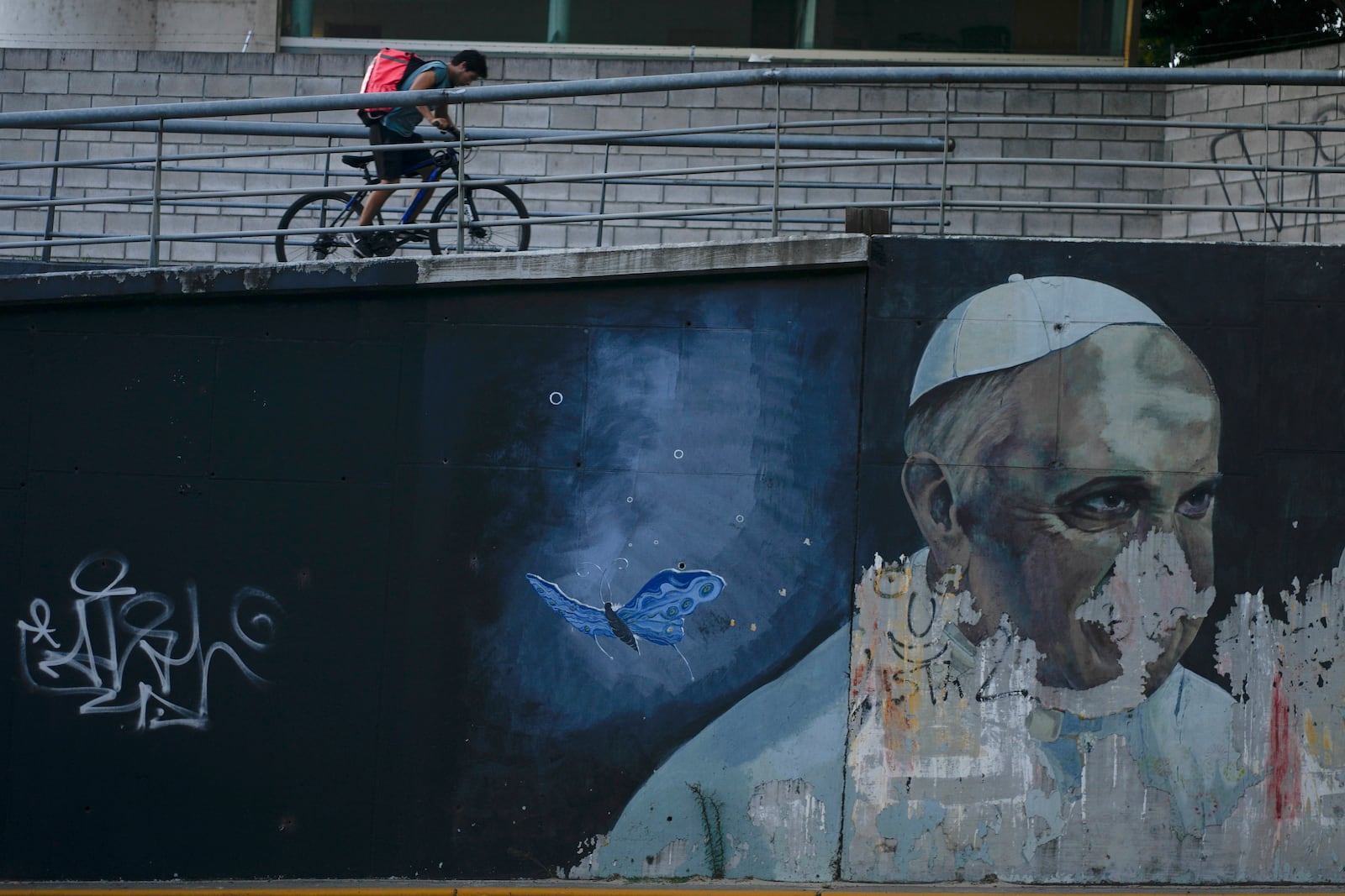 FILE - A man rides a bicycle near a weathered mural of Pope Francis in Buenos Aires, Argentina, March 2, 2023. (AP Photo/Natacha Pisarenko, File)
