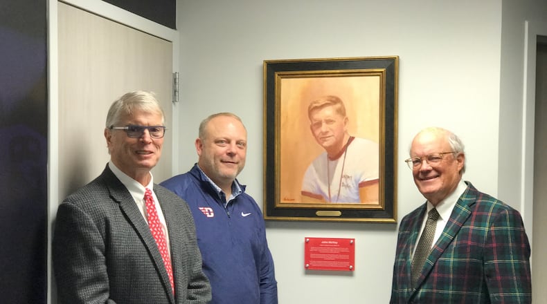 From left, UD Hall of Fame football player, noted orthopedic surgeon and former Dayton Flyers team doctor, Dr, Tum Quinn, current UD football coach Trevor Andrews and local artist Greg Gibson, pose around  portrait of former University of Dayton football coach John McVay that Gibson did and which was just hung in UD football offices last week.