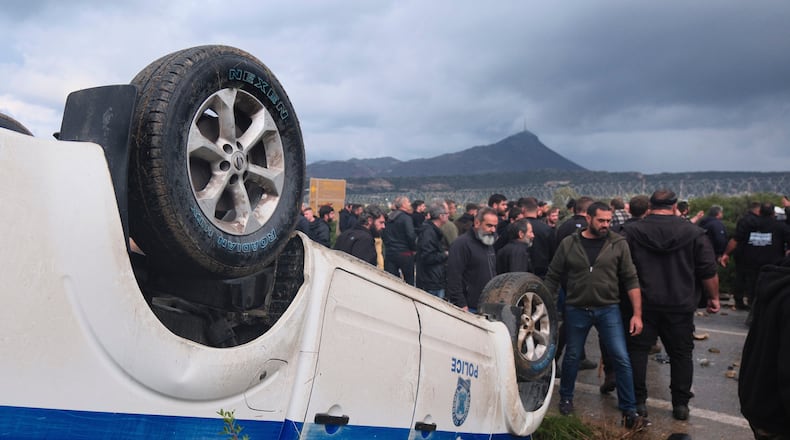 Farmers gather next to an overturned police vehicle during clashes with officers blocking their march to Chania's airport on Crete, Greece, Monday, Dec. 8, 2025, amid protests over delayed EU farm subsidies. (AP Photo/Giannis Angelakis)