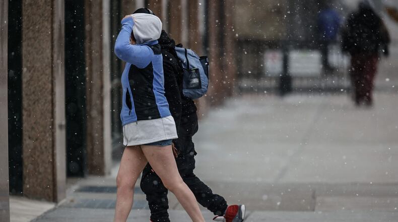 Weather optimistic pedestrians walk in downtown Dayton on the first cold, snowy and blustery day Monday December 18, 2023. JIM NOELKER/STAFF