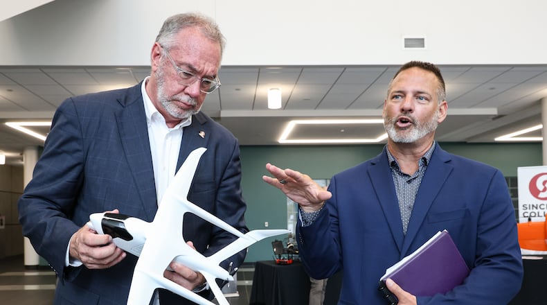 Sinclair Community College Senior Vice President Jeffery Millern (right) talks on Wednesday, Aug. 13 at Ned J. Sifferlen Health Sciences Center as Sinclair President Steven Johnson (left) holds the model of an aircraft the college is purchasing. The aircraft is expected to be delivered in early 2026. BRYANT BILLING / STAFF
