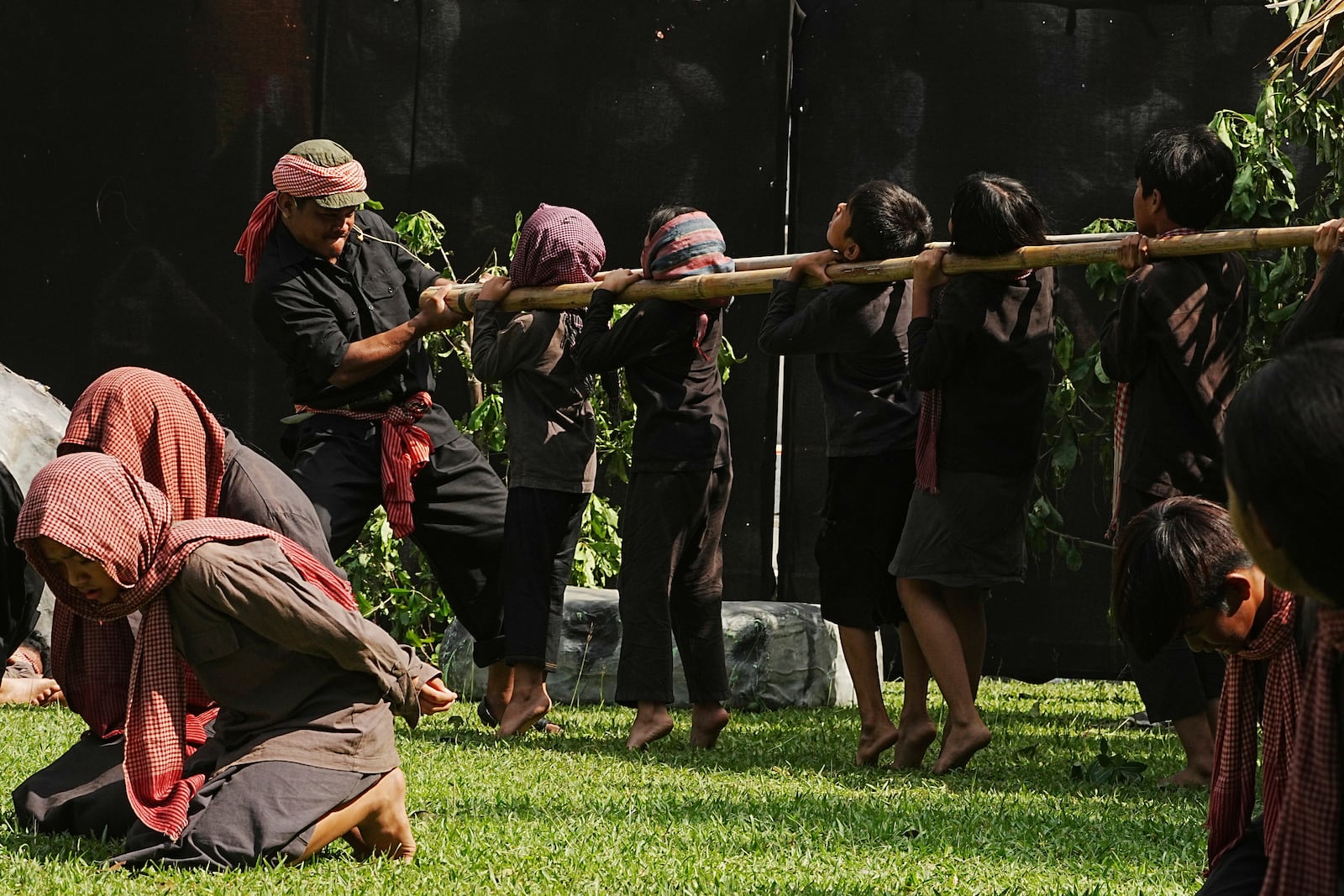 Cambodian students from Royal University of Fine Arts reenact a torture, with children being put on bamboo around their necks by the Khmer Rouge during their reign of terror in the 1970s in an event hosted by the ruling Cambodian People's Party to mark the annual of Remembrance Day at Choeung Ek, a former Khmer Rouge "killing field," on the outskirt of Phnom Penh, Cambodia Tuesday, May 20, 2025. (AP Photo/Heng Sinith)