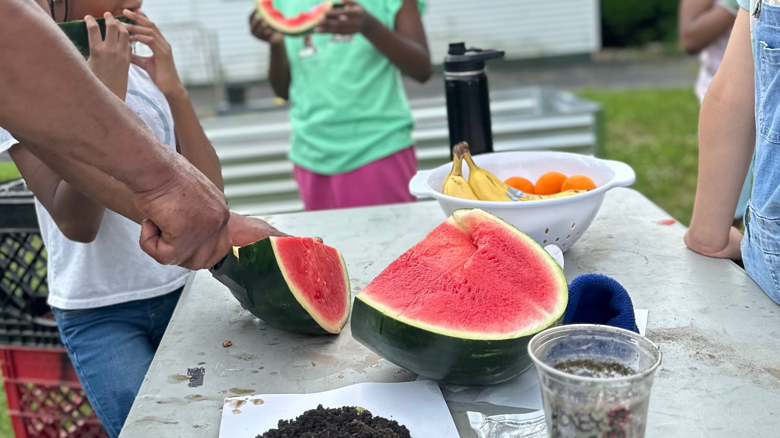 DeVann Carter slicing watermelon in front of children who are a part of his weekly garden youth club. Surrounding children try the watermelon. CONTRIBUTED