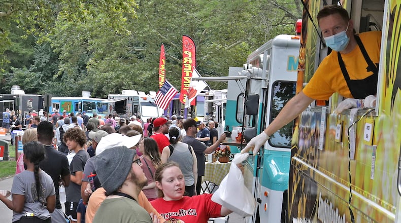 Hundreds of people walk up and down Cliff Park Drive eating from food trucks and watching Ohio State on a jumbotron screen Saturday during the Springfield Rotary Gourmet Food Truck Competition. BILL LACKEY/STAFF