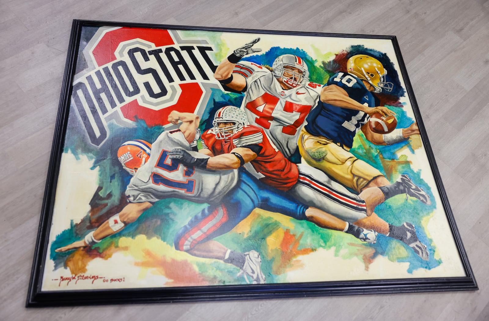 Gary Blevin's painting of former Ohio State linebacker A. J. Hawk tackling Illinois quarterback Tim Brasic, left, and Notre Dame quarterback Brady Quinn, right, rests on a surface in Blevin's art gallery on Thursday, Dec. 18, 2025, in Springfield. JOSEPH COOKE/STAFF