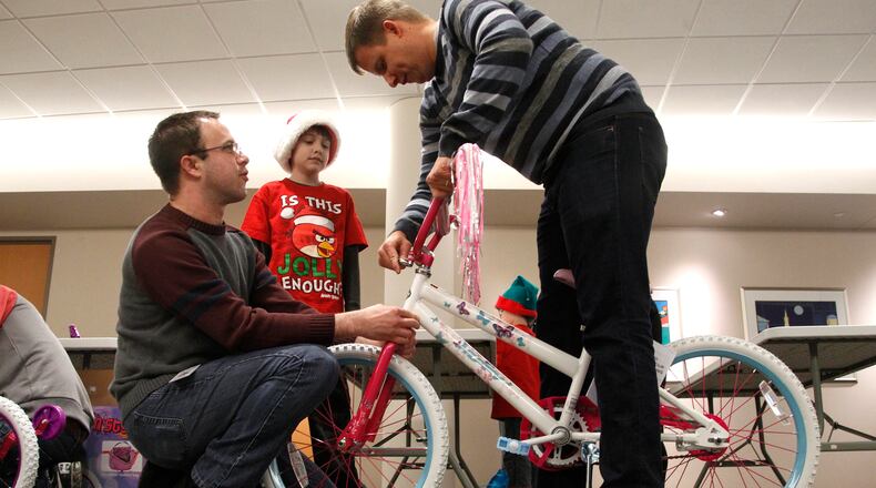 Reynolds and Reynolds’ annual bike-build event is Saturday. In this 2014 photo, Chris Brown (left) and co-worker Matt Owens (right) assemble a bike with the help of Owen’s son Aidan, then 11. LISA POWELL / STAFF PHOTO
