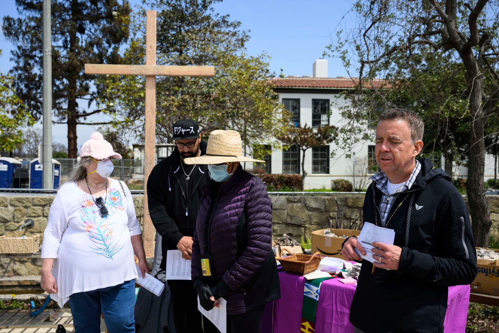Members of a church listen to a prayer by Pastor John Shaver, right, during a Cross Walk event by the Community United Methodist Church of the Pacific Palisades, Friday, April 18, 2025, in the Pacific Palisades area of Los Angeles. (AP Photo/William Liang)