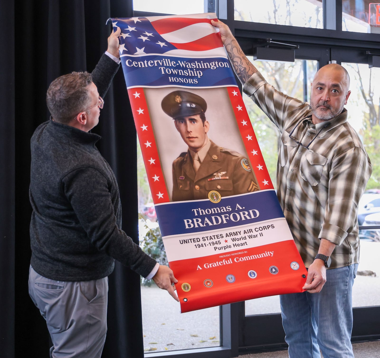 Army veteran Tony Miltenberger (left) and Army veteran Tim Pennartz hold a banner during a Veterans Day event on Tuesday, Nov. 11 at Benham's Grove in Centerville. Banners honoring local veterans will be hung in Stubbs Park. BRYANT BILLING/STAFF