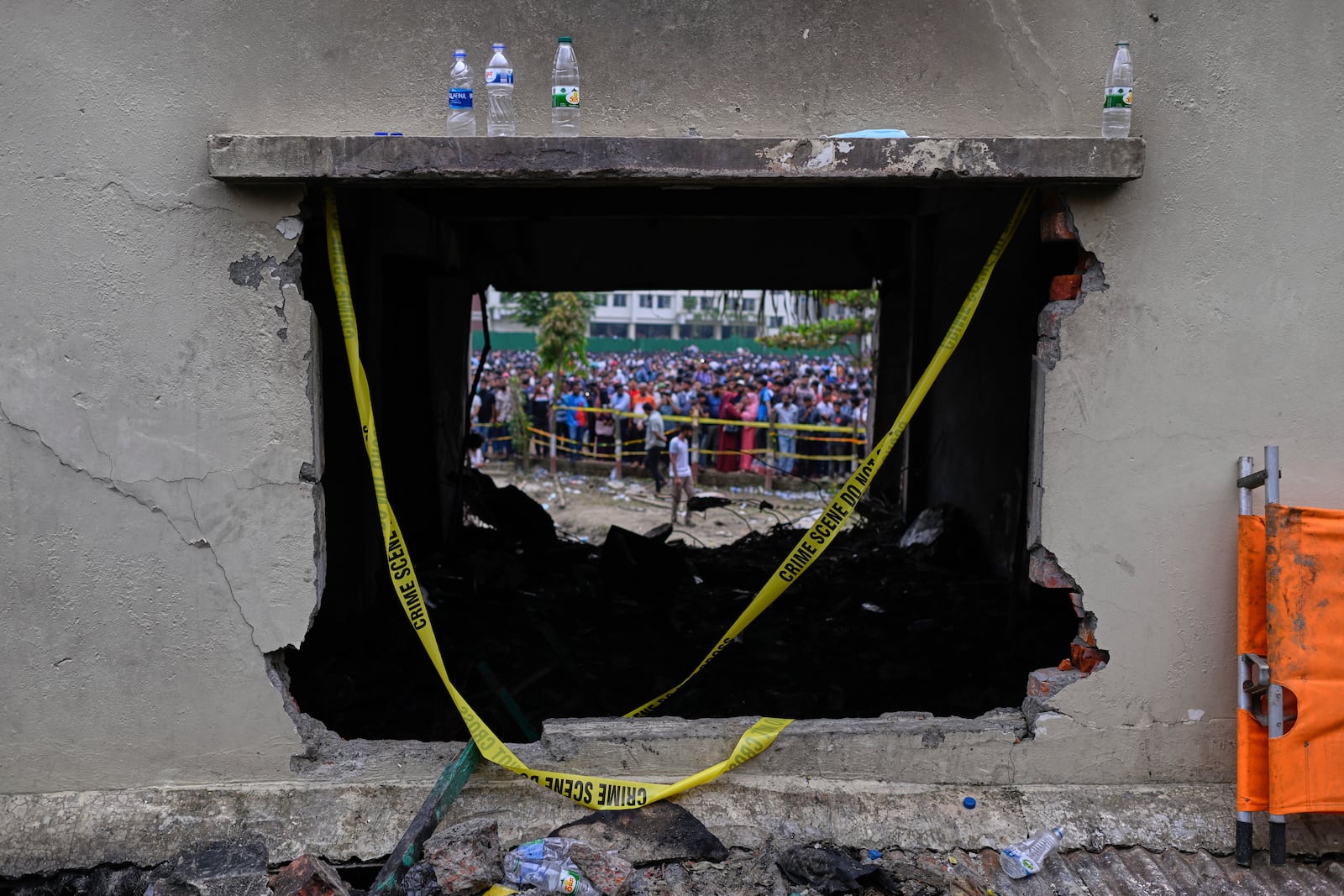 Onlookers are seen through a burnt classroom window of a school building after a Bangladesh air force training jet crashed into it Monday in Dhaka, Bangladesh, Tuesday, July 22, 2025. (AP Photo/Mahmud Hossain Opu)
