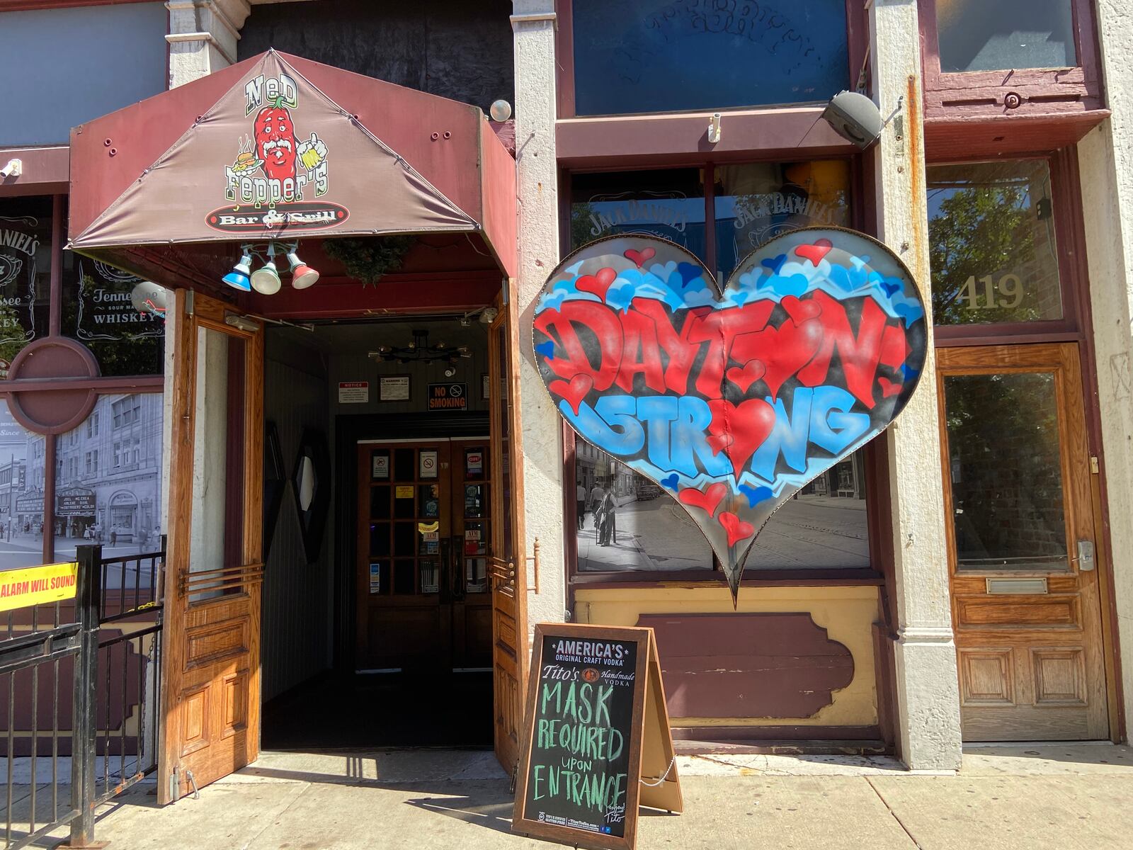 The Dayton Strong sign still stands outside Ned Peppers near the scene of the Aug. 4, 2019, mass shooting in the Oregon District, along with a sign that tells people to wear masks. Kaylee Harter/Staff
