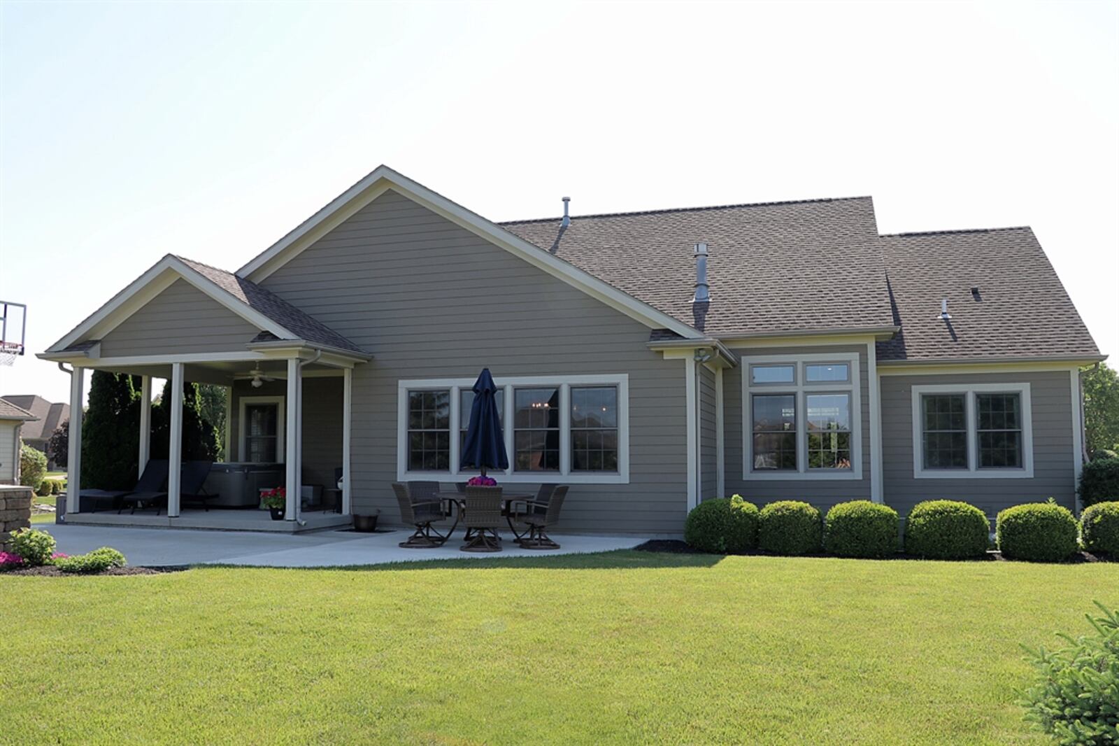 The porch has a ceiling paddle fan and extends out to a custom fire pit and grilling area. A concrete sun patio extends off the porch and is surrounded by landscaping.