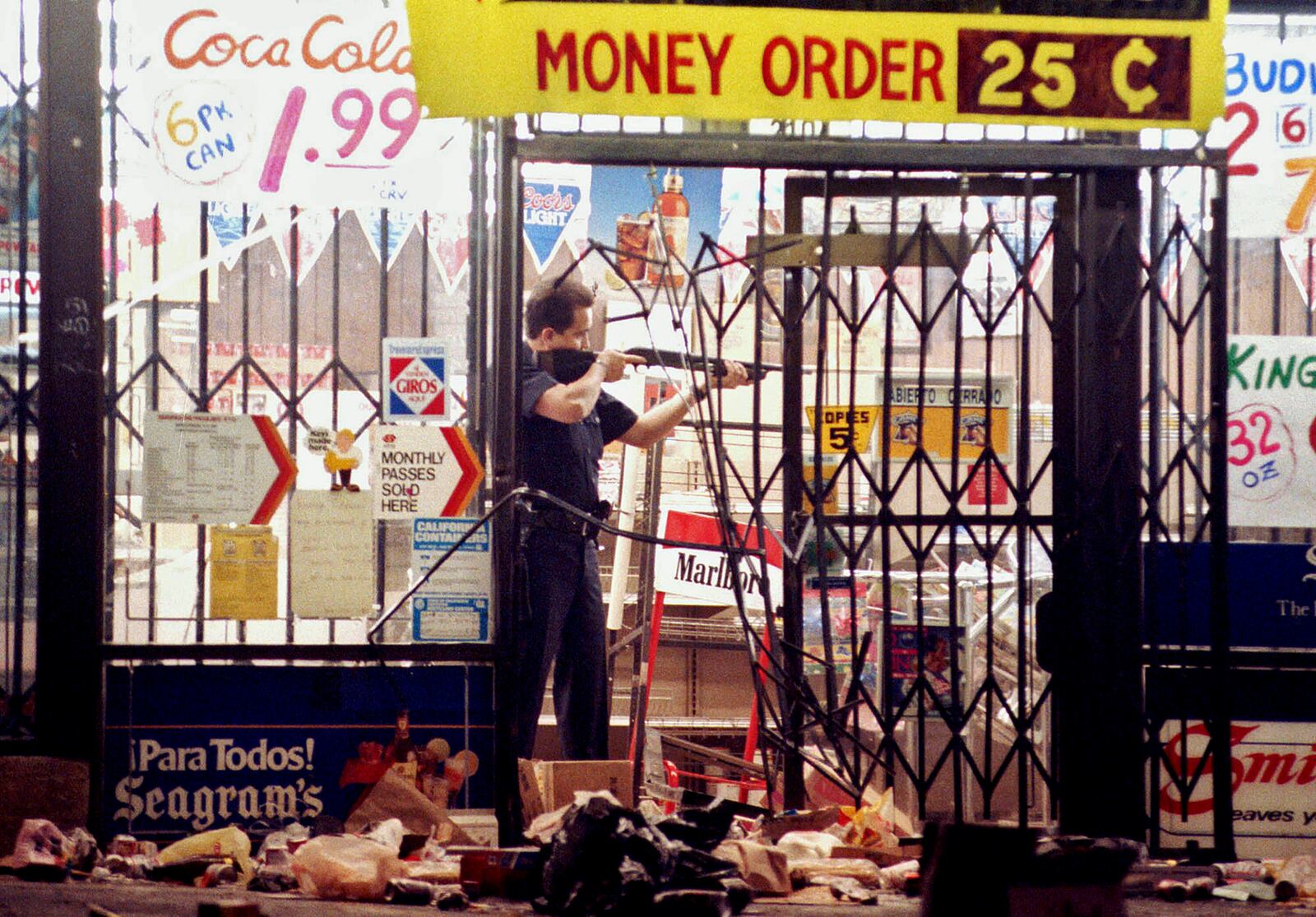 FILE - In this April 30, 1992 file photo, a Los Angeles police officer takes aim at a looter in a market at Alvarado and Beverly Boulevard in Los Angeles during the second night of rioting in the city. (AP Photo/John Gaps III, File)