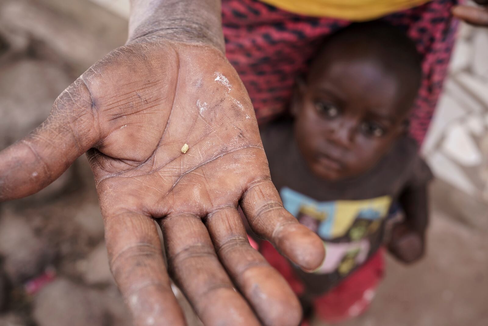 Sadio Camara's son clings to her as she holds a crumb of gold she extracted using mercury at her home in the Kedougou region of Senegal on Thursday, Jan. 16, 2025. (AP Photo/Annika Hammerschlag)