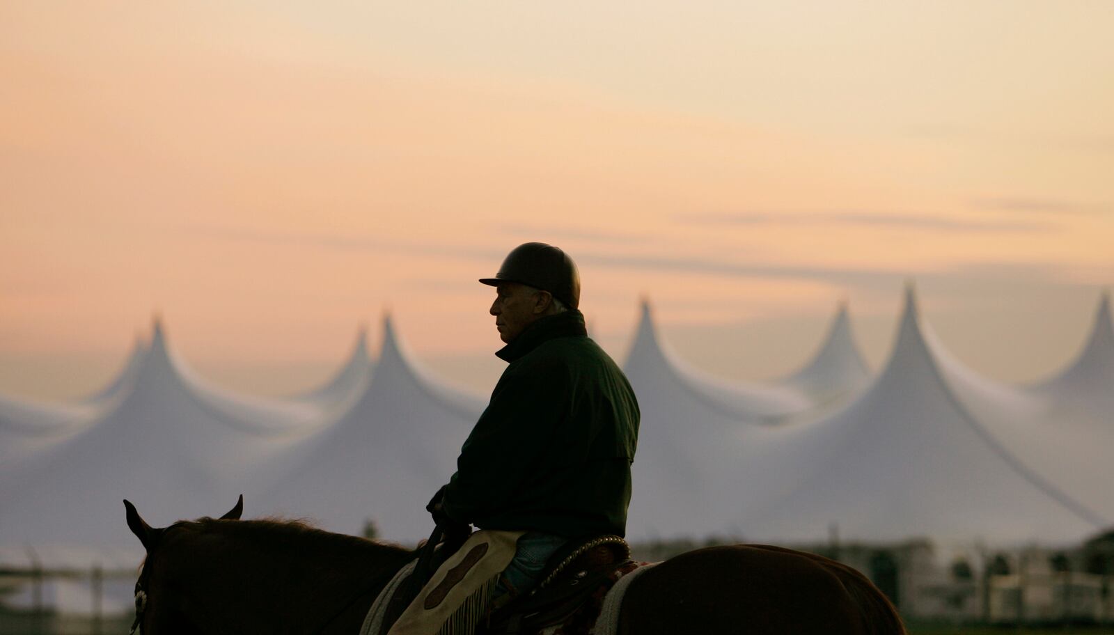 FILE - Trainer D. Wayne Lukas sits atop his horse as he watches morning workouts against the backdrop of a large tent set up in the infield before sunrise at Churchill Downs in Louisville, Ky., April 25, 2009. (AP Photo/Ed Reinke, file)