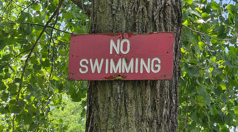 A no swimming sign attached to a tree along a trail of Madison Lakes Park in Montgomery County Ohio.