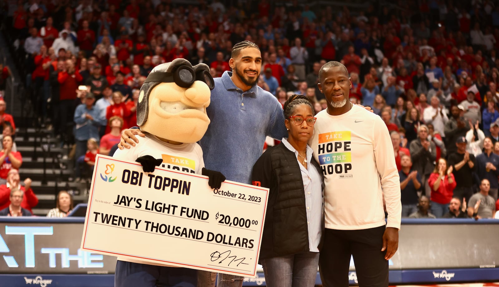 Former Dayton star Obi Toppin, second from left, gives a check for $20,000 to Dayton coach Anthony Grant, right, and his wife Chris during an exhibition game against Ohio State on Sunday, Oct. 22, 2023, at UD Arena. David Jablonski/Staff