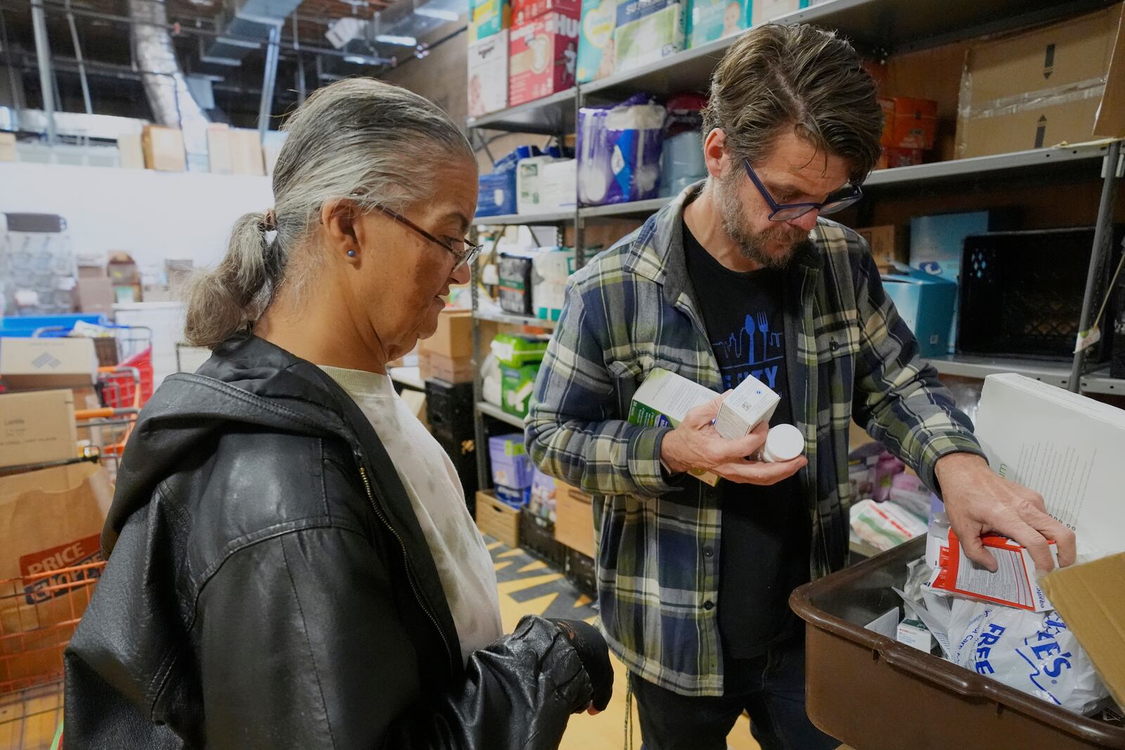 Pantry director Christopher Lowrance looks for items requested by Beth Anne Mollett, left, at the Bishop Sullivan Center food pantry, Tuesday, April 15, 2025, in Kansas City, Mo. (AP Photo/Charlie Riedel)