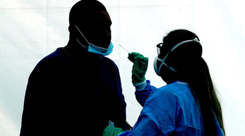 A man is silhoutted against the wall of a white tent, illuminated by the sun, as he gets a COVID-19 test at the Clark County Combined Health District's free COVID testing clinic at Hayward Middle School.
