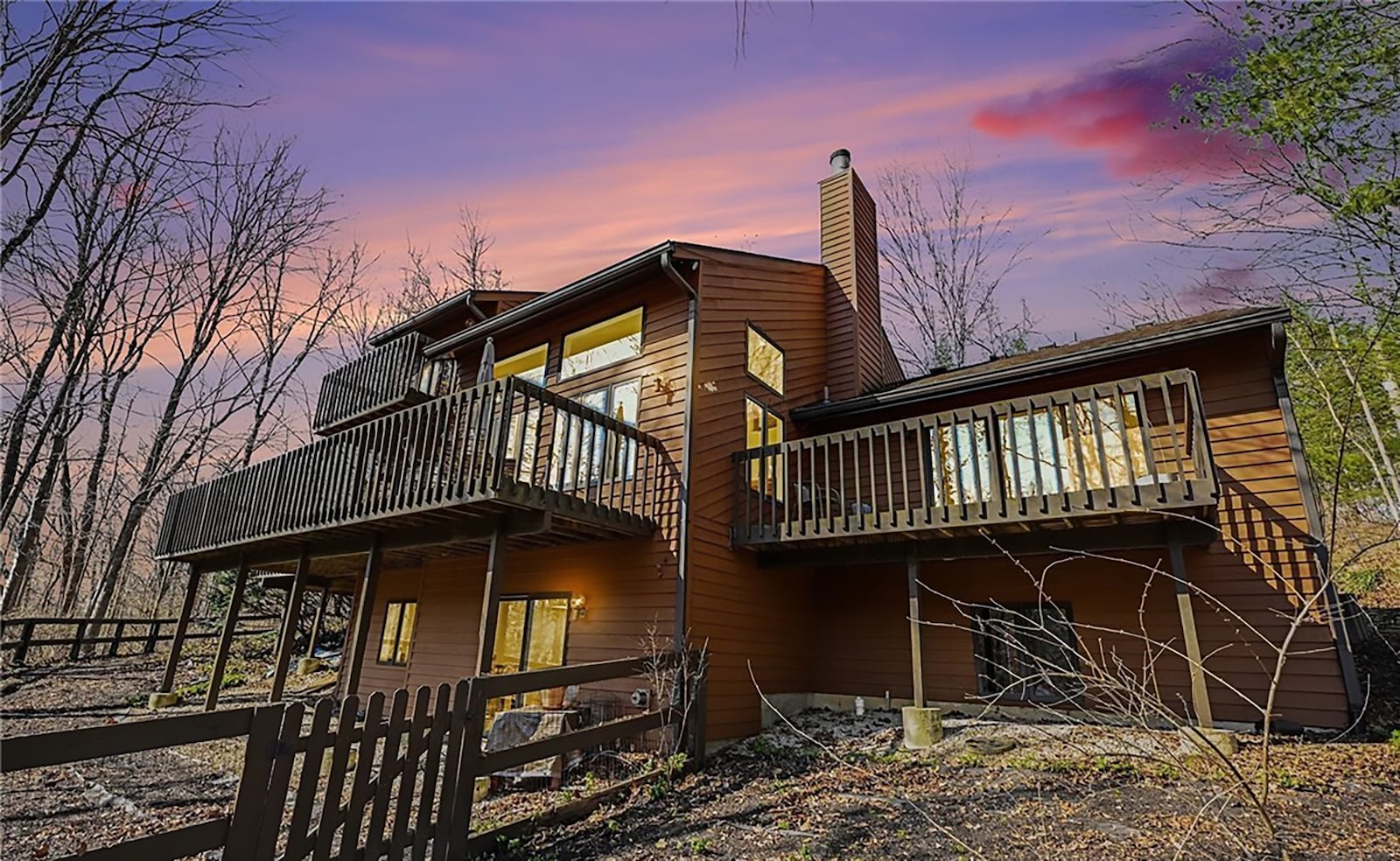 The back of the house features a partial fence and a multilevel system of wood decks with railings and steps. The lot is heavily wooded. CONTRIBUTED
