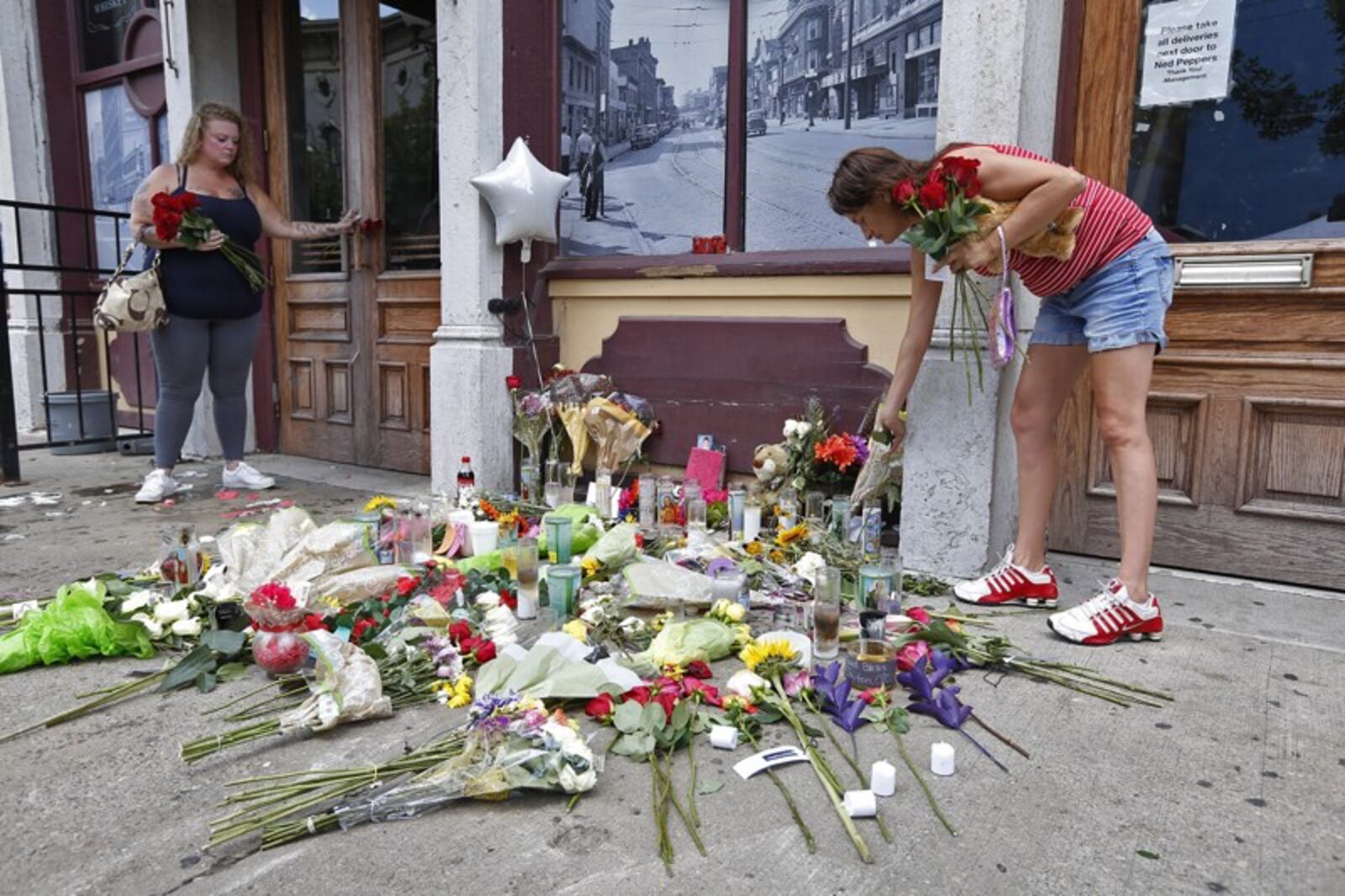 Natalie Driscoll, left, and Amber Lannon place flowers for shooting victim Derrick Fudge along East Fifth Street on Monday. TY GREENLEES / STAFF