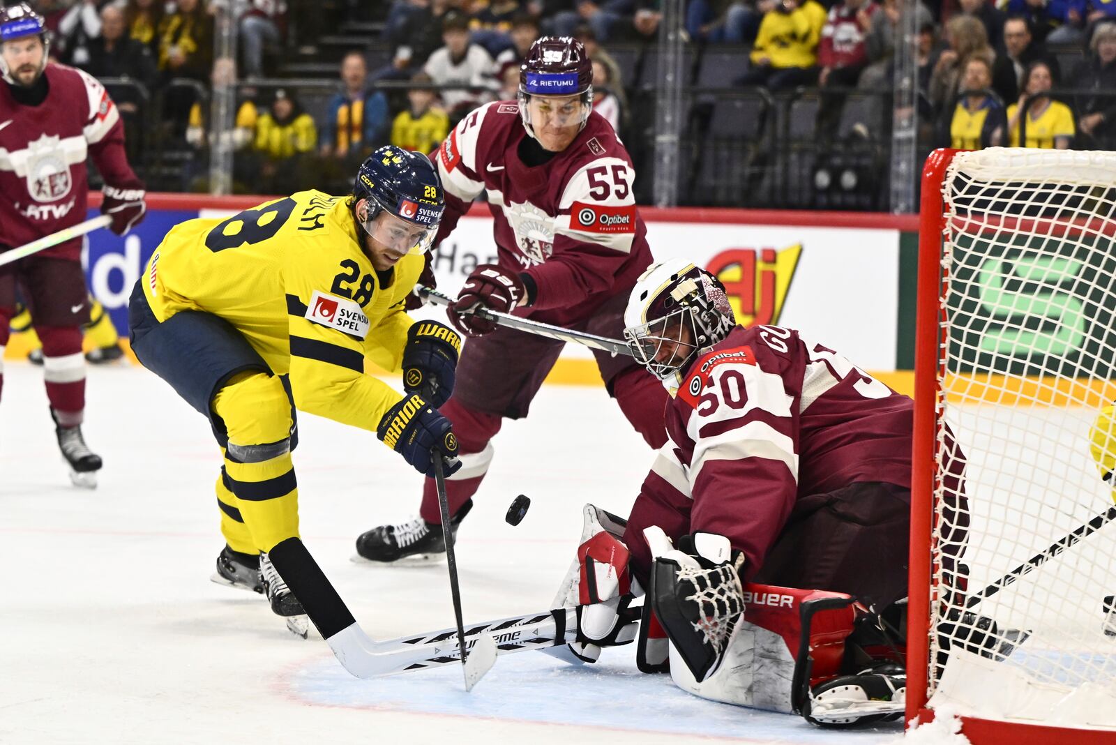 Latvia's Roberts Mamcics, center, and goalkeeper Kristers Gudlevskis, right, challenge for the puck with Sweden's Elias Lindholm, left, during the IIHF Ice Hockey World Championship group A match between Latvia and Sweden in Stockholm, Sweden, Wednesday, May 14, 2025. (Anders Wiklund/TT News Agency via AP)