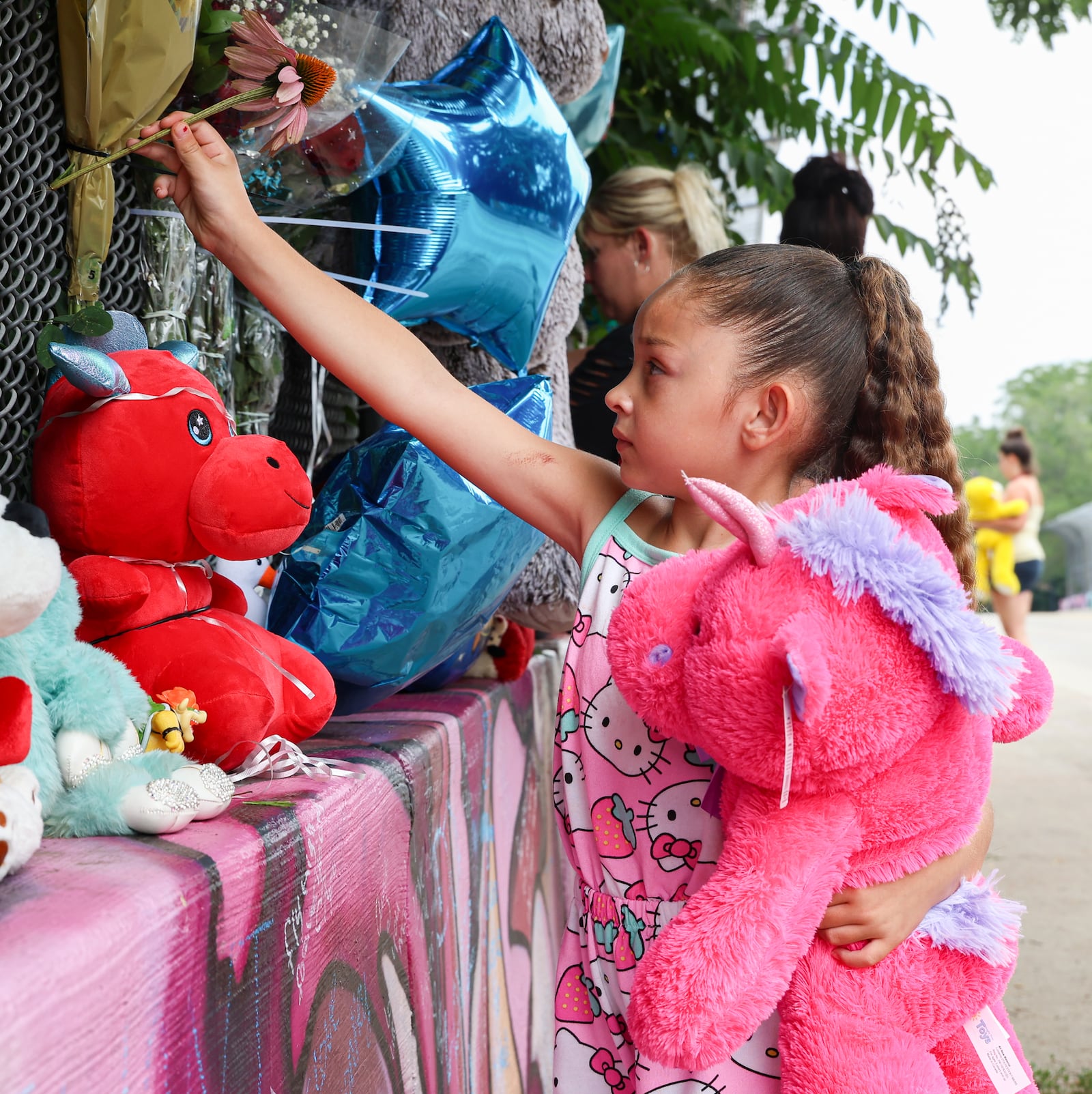 Isabella Tojin places a purple coneflower in fencing on a bridge on McClure Street in Dayton on Monday, July 14, 2025. She and her family left stuffed animals and flowers at a roadside memorial for 7-year-old Hershall Creachbaum, who was believed to be found dead on Saturday, July 12, 2025. Michael Kendrick, who is dating Creachbaum’s mother, is facing three counts of tampering with evidence and one count of gross abuse of a corpse. BRYANT BILLING / STAFF