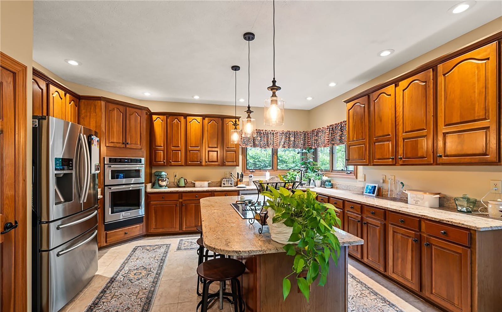 The kitchen has wood cabinets, an island with bar seating, granite countertops and appliances including a cooktop, wall oven, microwave, dishwasher and French door refrigerator.