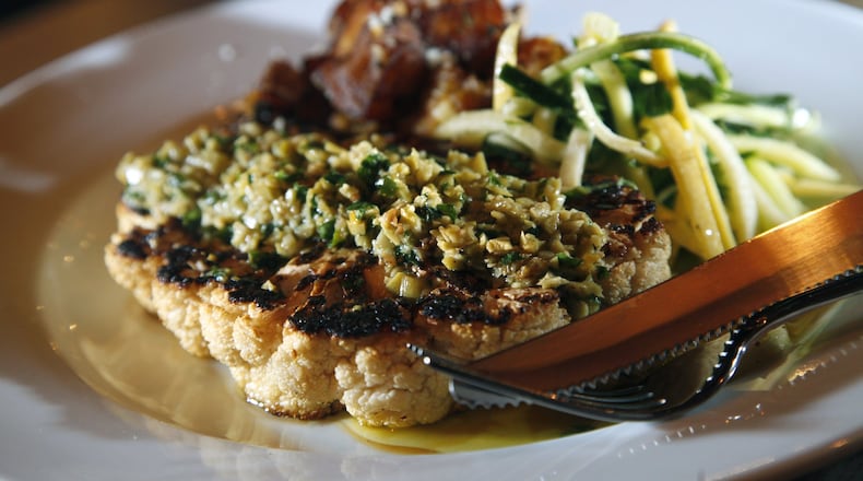 Wheat Penny Oven and Bar serves a caluliflower t-bone served with roasted potatoes and zucchini with mint. The t-bone is garnished with chopped sauce made of olive, garlic, capers, raisins, orange segments, herbs and olive oil. LISA POWELL / STAFF