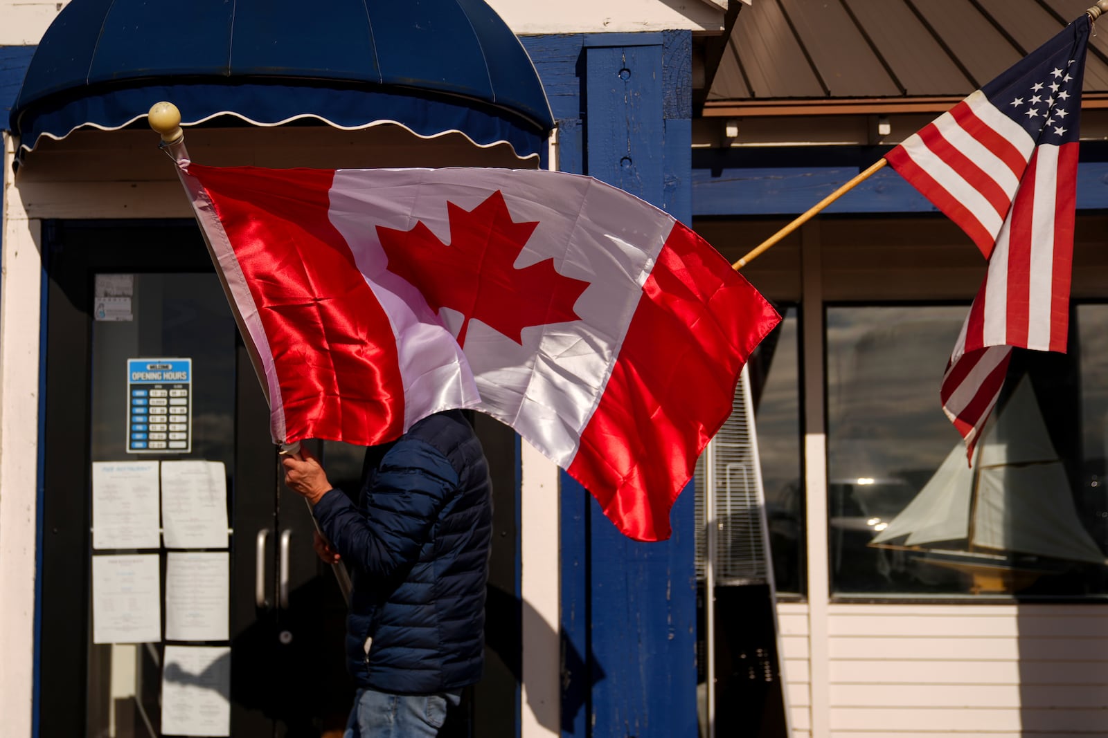 FILE - A worker at The Pier, one of three restaurants in town, readjusts Canadian and American flags hanging outside the business, Monday, March 17, 2025, in Point Roberts, Wash. (AP Photo/Lindsey Wasson, File)