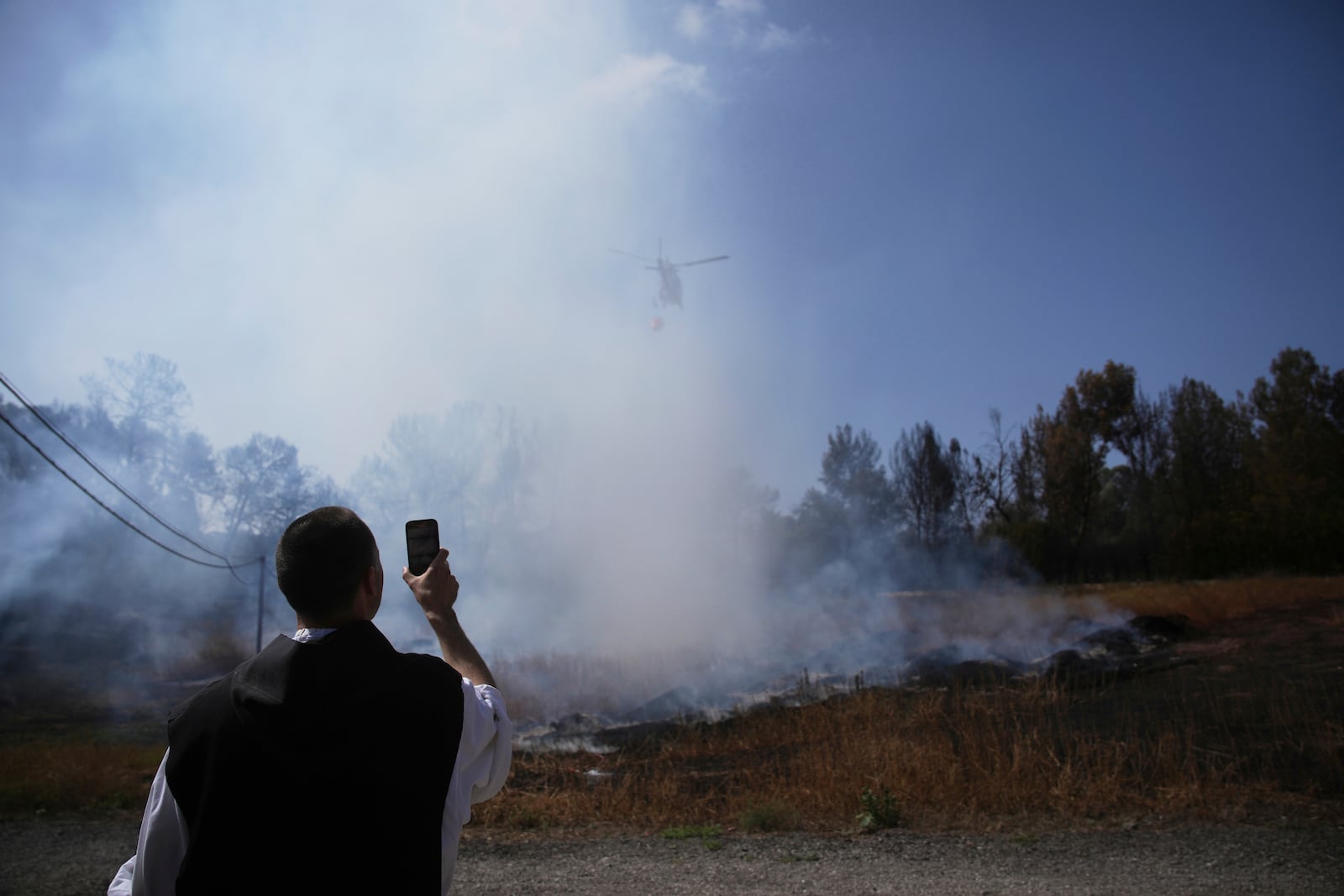 A Roman Catholic Trappist monk films an Israeli fire crew helicopter battling a wildfire outside his monastery in Latrun, Israel, outside of Jerusalem, Thursday, May 1, 2025. (AP Photo/Ohad Zwigenberg)