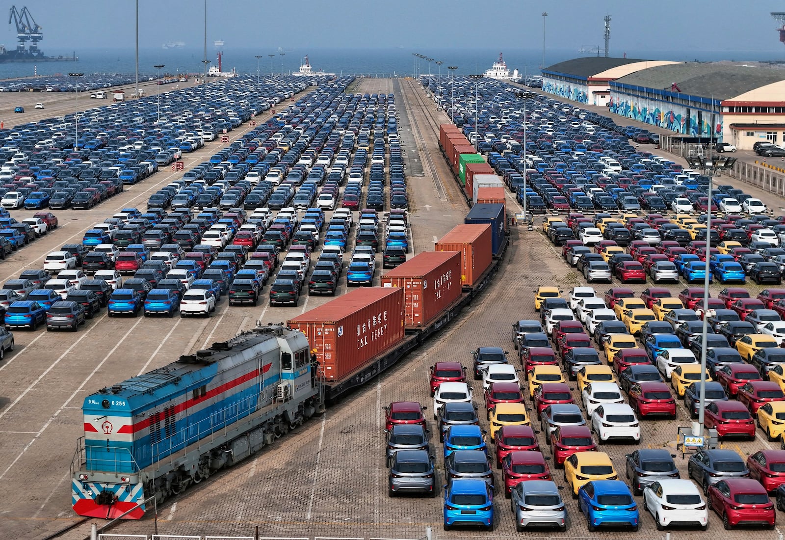 A cargo train moves past new cars waiting for shipment in a port, in Yantai in east China's Shandong province on Wednesday, May 7, 2025. (Chinatopix via AP)