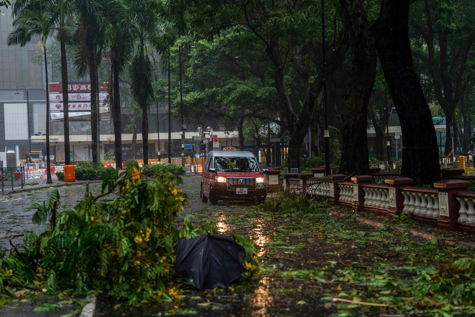 A taxi drives near fallen trees following the Typhoon Wipha, in Hong Kong, Sunday, July 20, 2025. (AP Photo/Vernon Yuen)