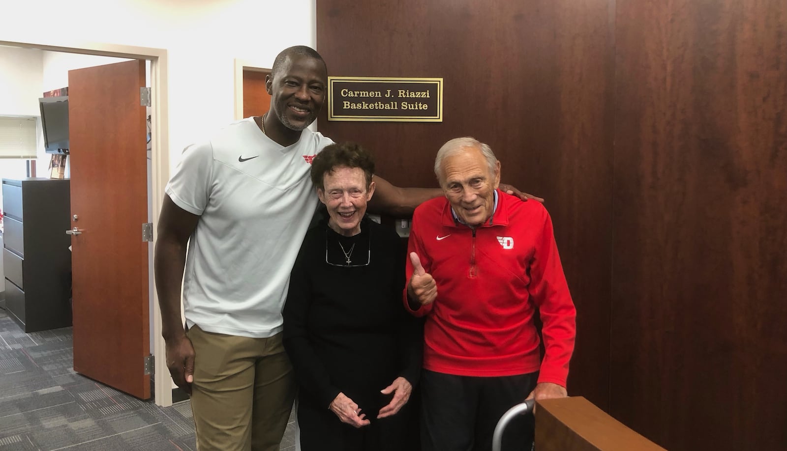 Carmen Riazzi, right, poses for a photo with his wife Ann and Dayton coach Anthony Grant at UD's Cronin Center. Contributed photo