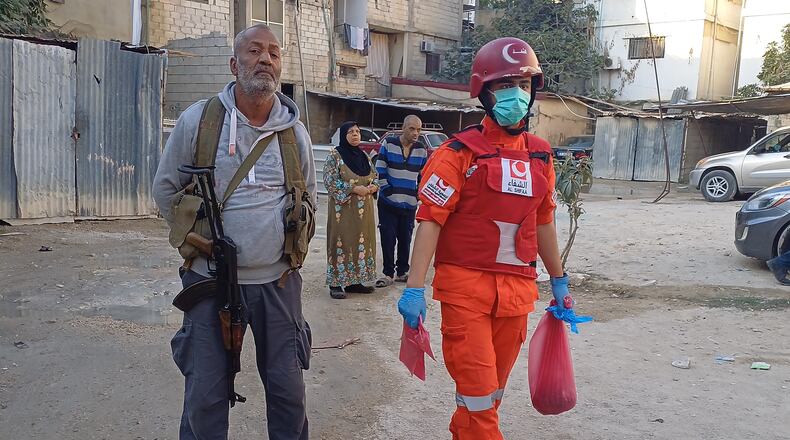 A Hamas gunman, left, stands next of a Palestinian rescue man who carries a bag with body remains, near the scene where an Israeli strike hit on Tuesday night the Ein el-Hilweh Palestinian refugee camp, in the southern port city of Sidon, Lebanon, Wednesday, Nov. 19, 2025. (AP Photo/Mohammed Zaatari)
