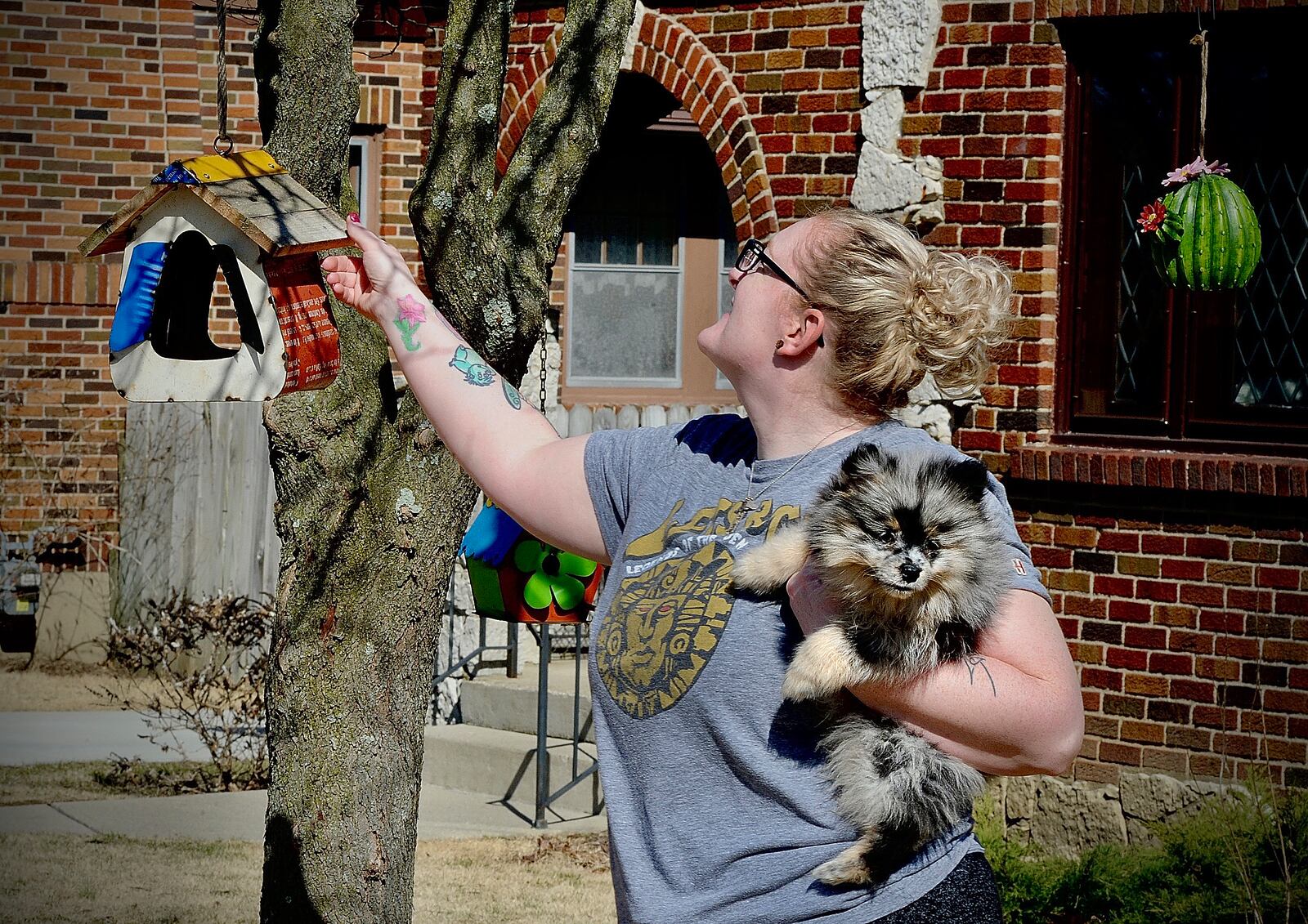 Christine Adams, with her 12 week old puppy, Pongo, hangs bird houses in a tree outside her home in Kettering, Wed. March 2, 2022. MARSHALL GORBY\STAFF