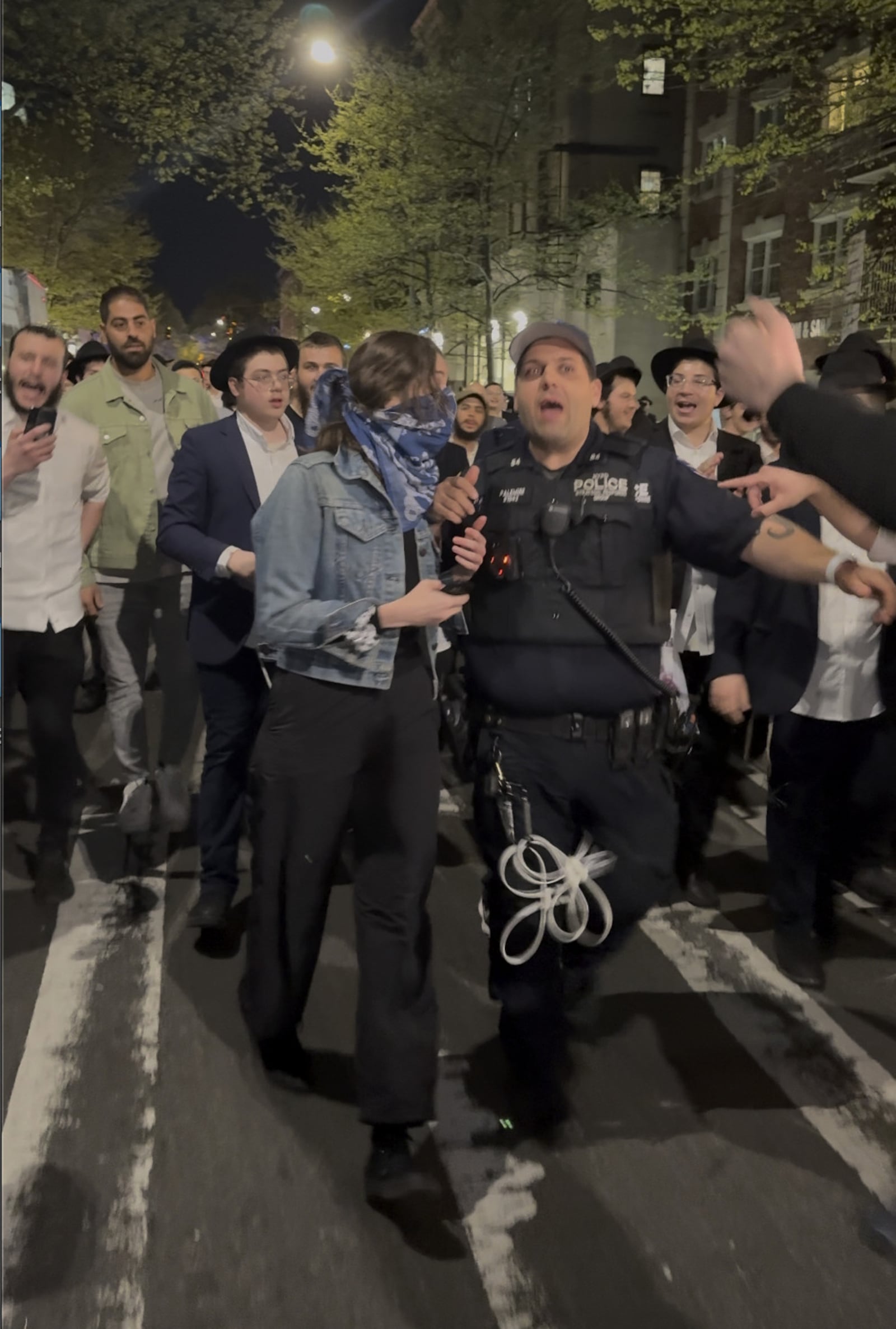 This image taken from video shows a woman and a police officer as they are pursued by a crowd of men in the Crown Heights section of Brooklyn, N.Y., on Thursday, April 24, 2025. (AP Photo)
