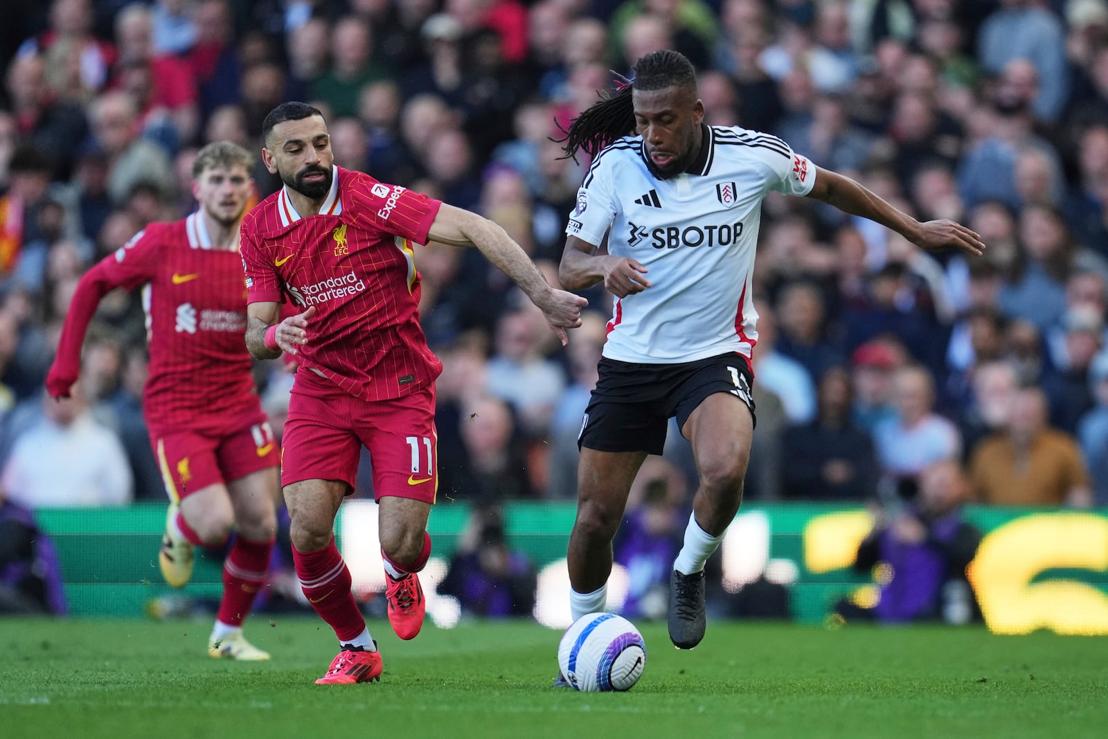 Fulham's Alex Iwobi, right, challenges for the ball with Liverpool's Mohamed Salah during the English Premier League soccer match between Fulham and Liverpool, at Craven Cottage, London, Sunday, April 6, 2025. (AP Photo/Kin Cheung)