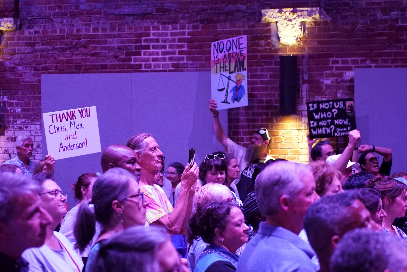 People wave signs during a Democratic town hall at the Haw River Ball Room in Saxapahaw, N.C., Thursday, April 24, 2025. (AP Photo/Allen G. Breed)