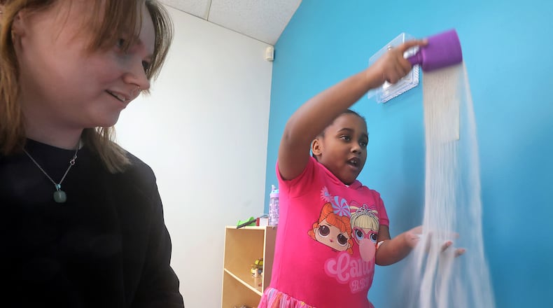 Ashley Brown, a mental health care provider at Kids Thrive, plays in a sand box with a child. BILL LACKEY/STAFF