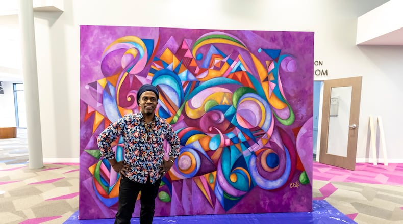 Cedric Michael Cox stands in front of the artwork he designed for the Dayton Metro Library's West branch. The colorful painting is entitled "Ascending Beyond." CONTRIBUTED