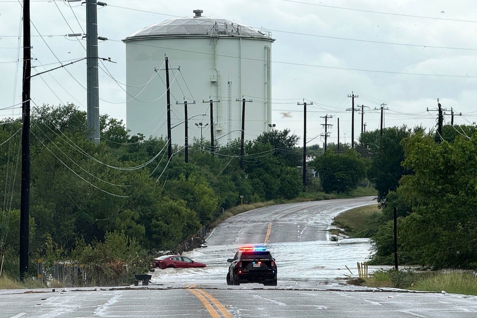 A police vehicle blocks a flooded roadway in San Antonio, Tx., where a vehicle was stranded after heavy rains in the city on Thursday, June 12, 2025. (AP Photo/Lekan Oyekanmi)