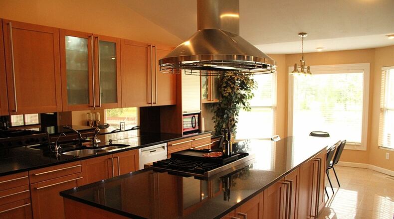 A seated bar in the kitchen doubles as one island with a prep sink and an under-counter beverage cooler. The long center island holds a four-burner slide-in gas range, then extends into the bay window area as a tiered breakfast bar with seating.