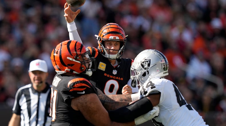 Cincinnati Bengals quarterback Joe Burrow, middle, passes as guard Cody Ford, left, blocks Las Vegas Raiders defensive end K'Lavon Chaisson during the first half of an NFL football game in Cincinnati, Sunday, Nov. 3, 2024. (AP Photo/Carolyn Kaster)